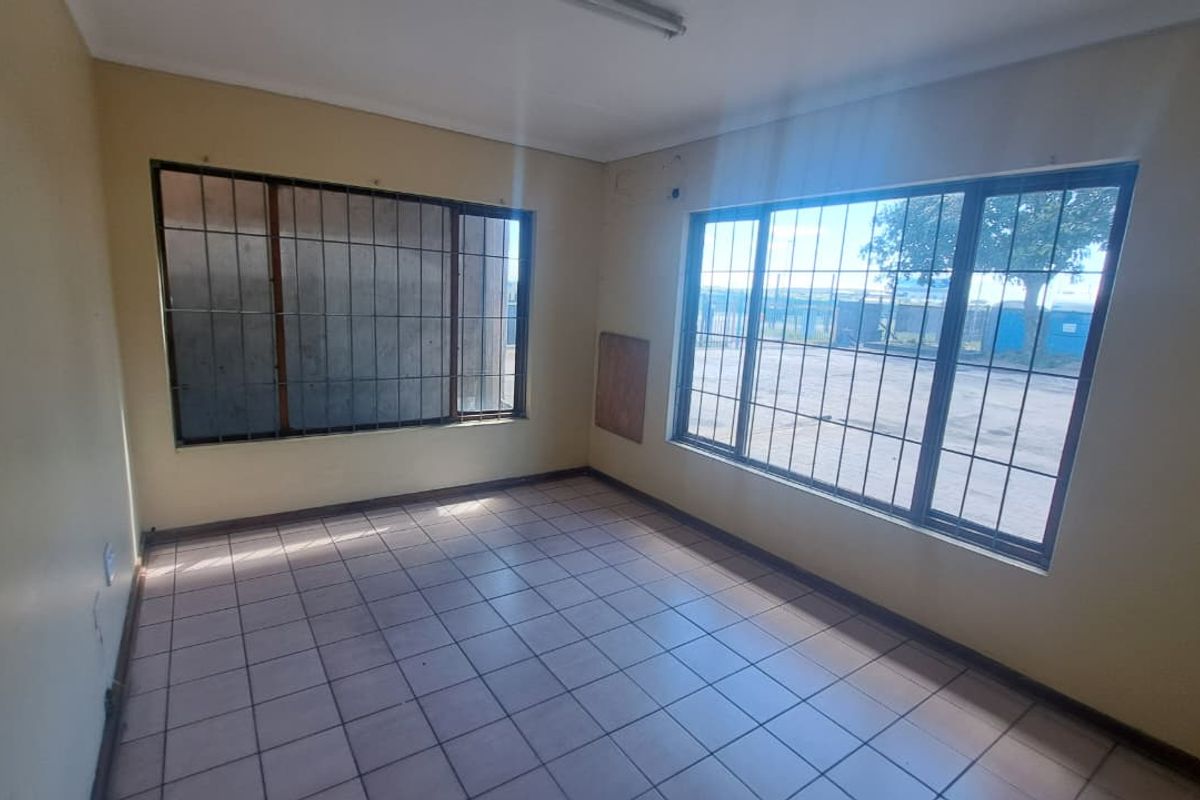 A vacant office space featuring tiled flooring, large windows with security bars, and neutral wall finishes, suitable for a professional workspace.