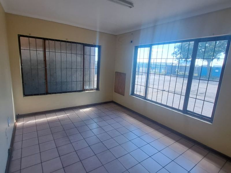 A vacant office space featuring tiled flooring, large windows with security bars, and neutral wall finishes, suitable for a professional workspace.