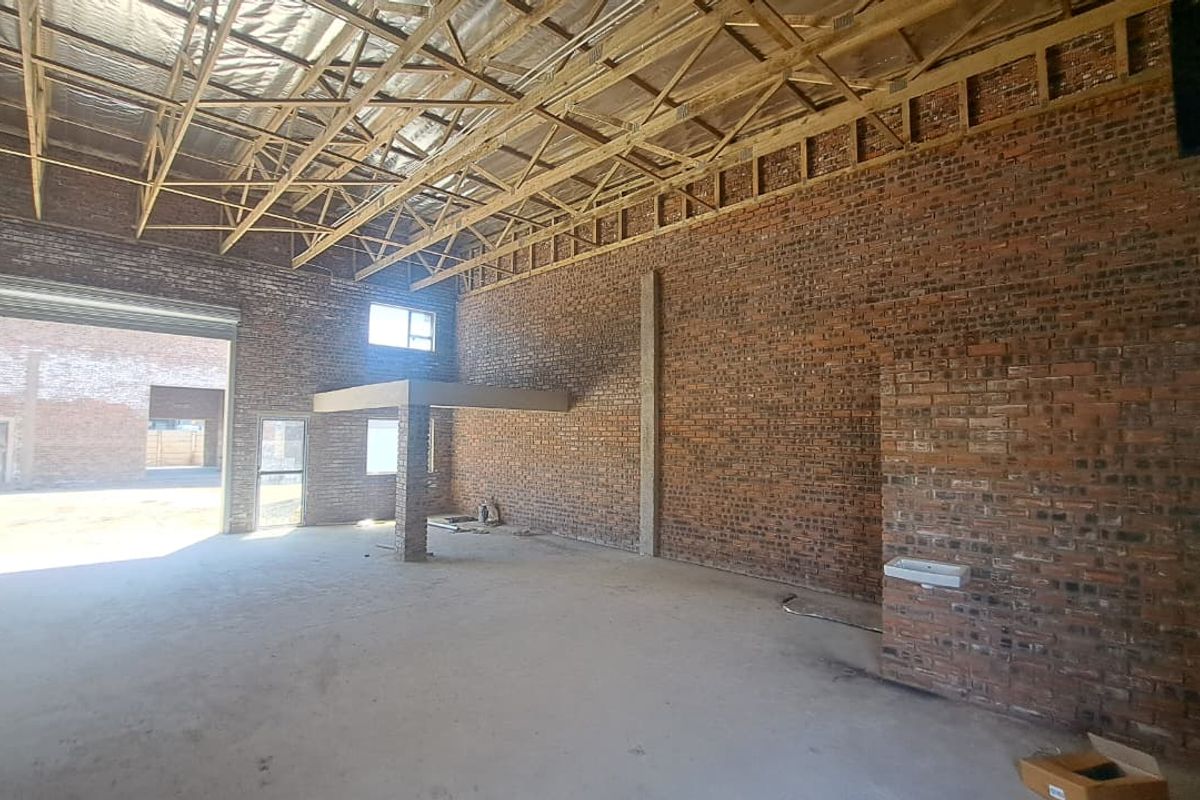 Spacious industrial unit featuring exposed brick walls, high timber truss ceilings, concrete flooring, a mezzanine level, and a roller shutter door for easy access.