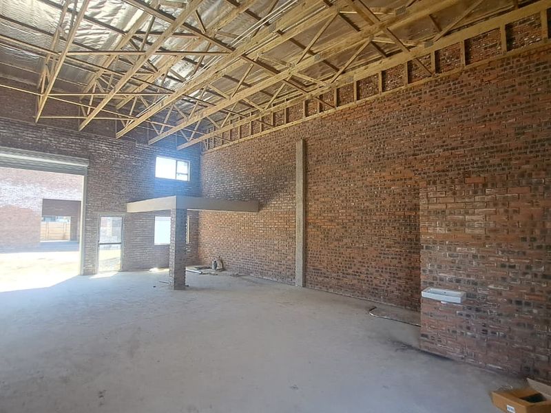 Spacious industrial unit featuring exposed brick walls, high timber truss ceilings, concrete flooring, a mezzanine level, and a roller shutter door for easy access.