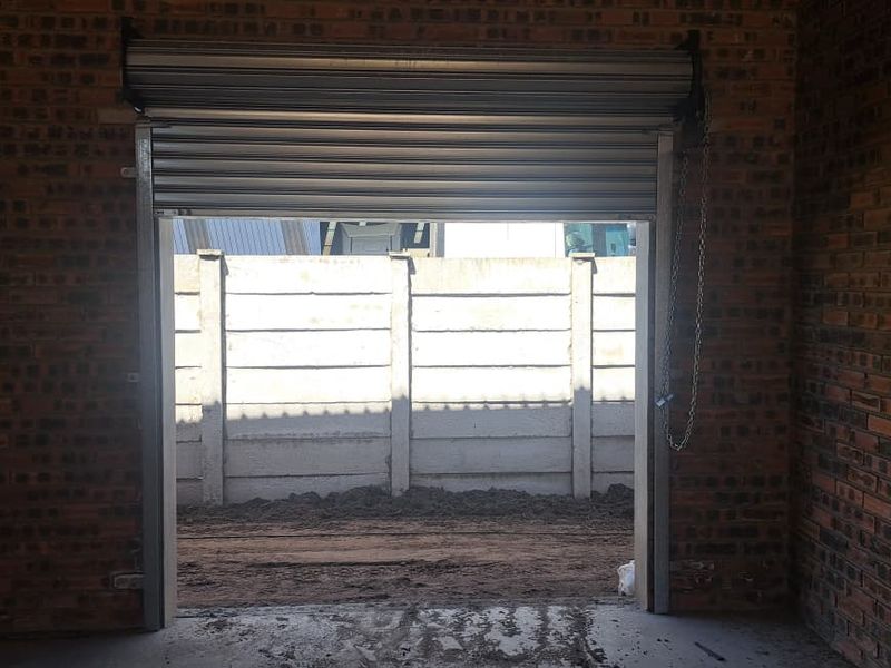 An industrial-style garage space featuring exposed brick walls, a concrete floor, and a functional roller shutter door opening to an outdoor area.