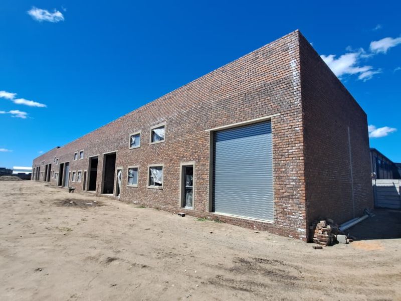 Industrial warehouse exterior featuring a face brick facade, large roller shutter door, and steel windows, set within an expansive, unfinished site.