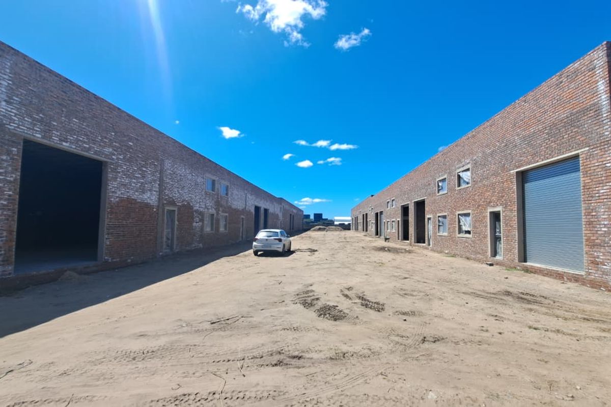 Exterior view of an industrial warehouse complex featuring exposed brick facades, multiple roller shutter doors, and an unpaved yard area.