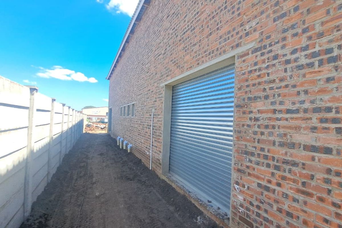 Rear exterior view of an industrial building featuring exposed brickwork, a secure roller shutter door, and a precast concrete boundary wall.