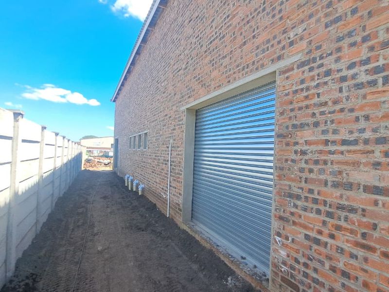 Rear exterior view of an industrial building featuring exposed brickwork, a secure roller shutter door, and a precast concrete boundary wall.