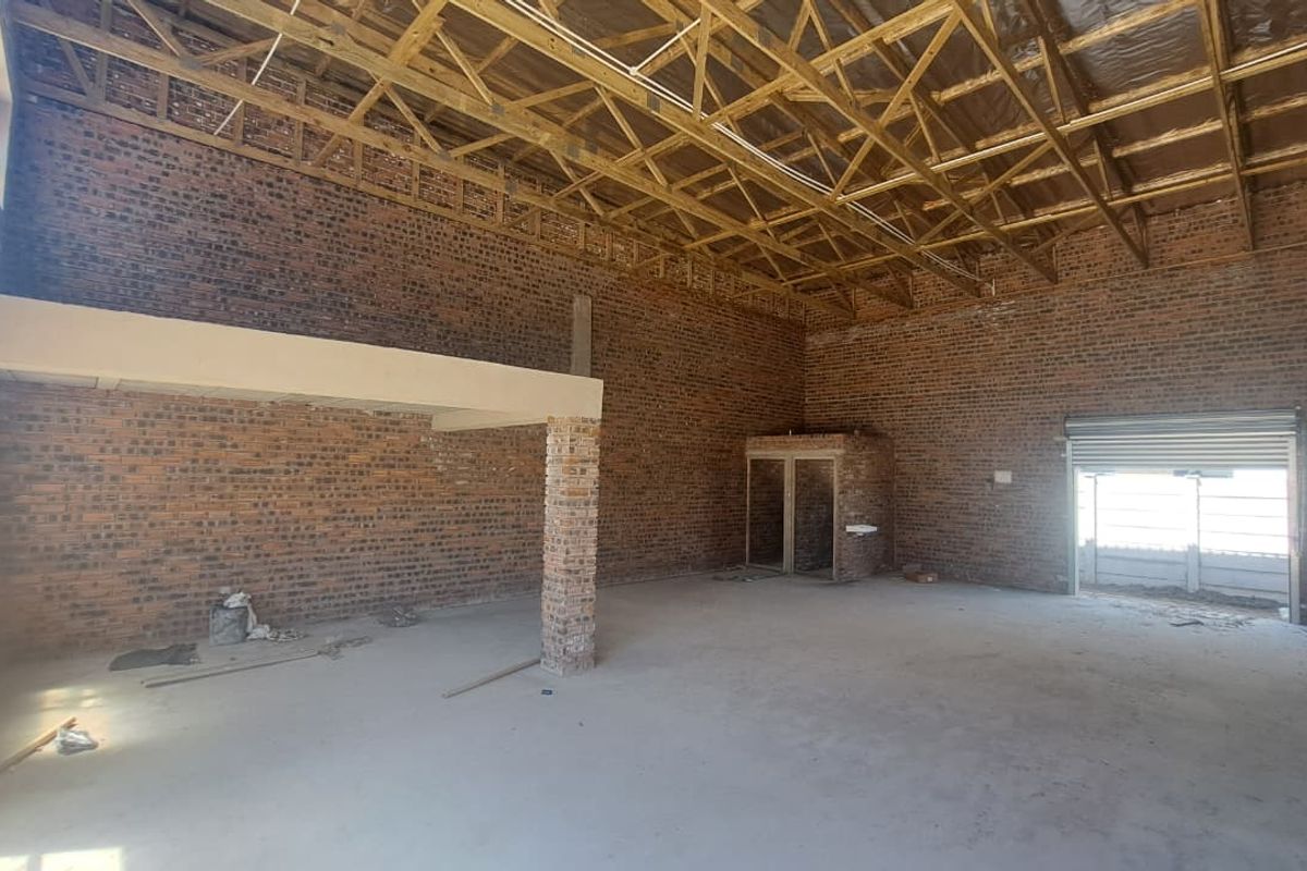 Spacious industrial utility area featuring exposed brick walls, timber roof trusses, a concrete floor, and a roller shutter door, suitable for various commercial applications.