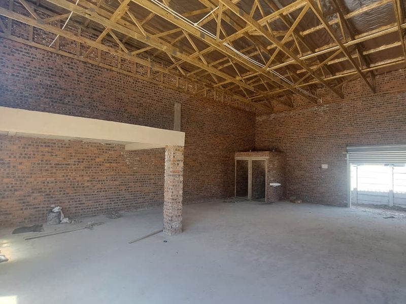 Spacious industrial utility area featuring exposed brick walls, timber roof trusses, a concrete floor, and a roller shutter door, suitable for various commercial applications.