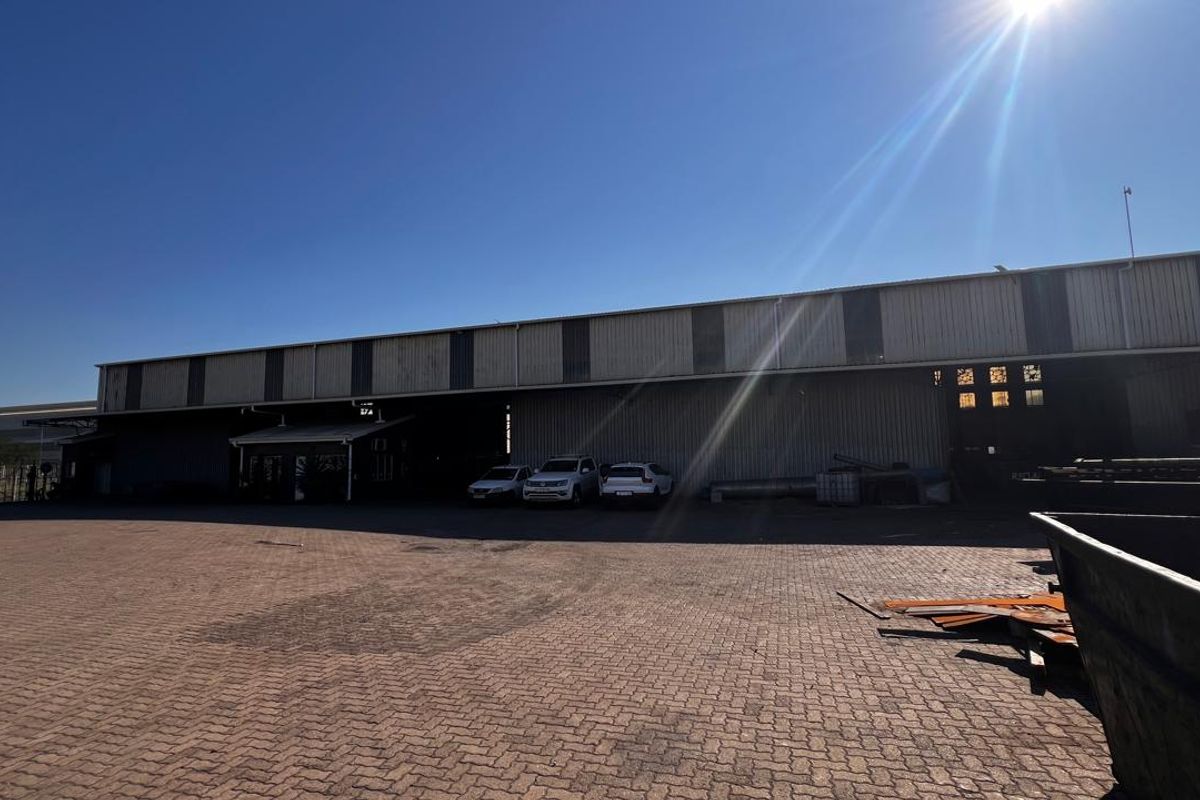 Industrial property exterior featuring a large paved yard area and corrugated metal warehouse structure with multiple access points.