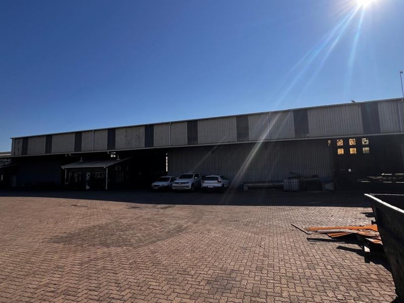 Industrial property exterior featuring a large paved yard area and corrugated metal warehouse structure with multiple access points.