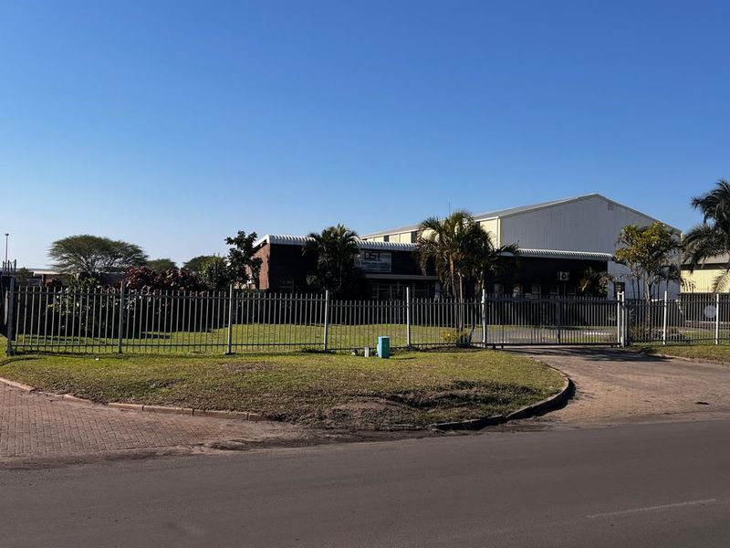 Front view of an industrial property featuring a secure gated entrance, paved driveway, and warehouse building with perimeter fencing.