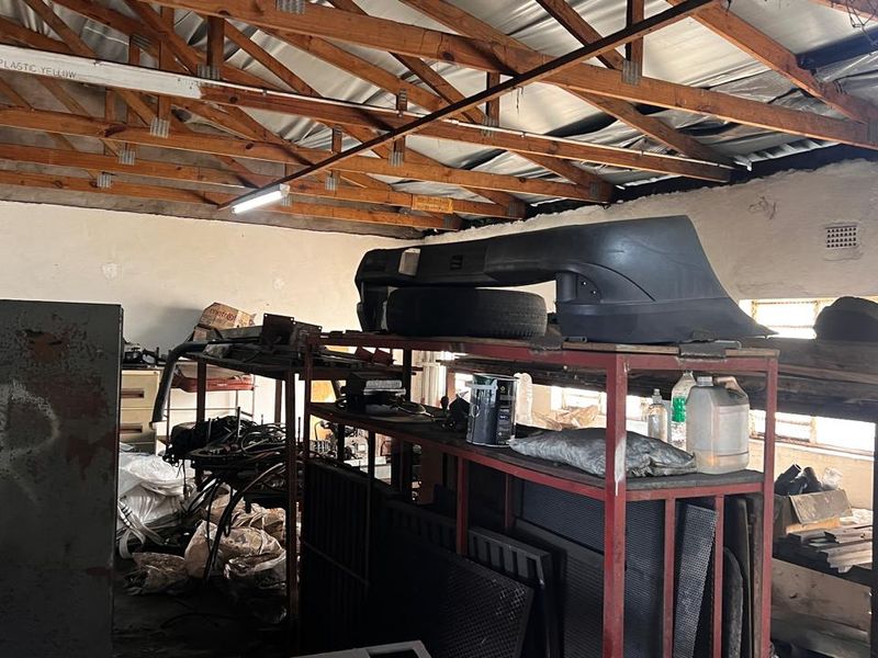 Industrial utility space featuring exposed timber roof trusses, corrugated metal roofing, and functional ventilation, suitable for storage or workshop use.