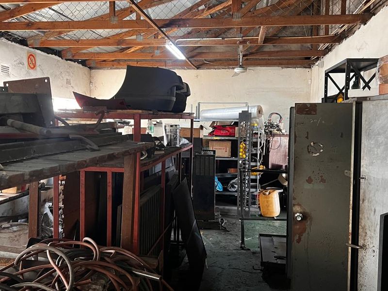 Industrial utility space featuring exposed timber roof trusses, concrete flooring, and fluorescent lighting, suitable for storage or workshop use.