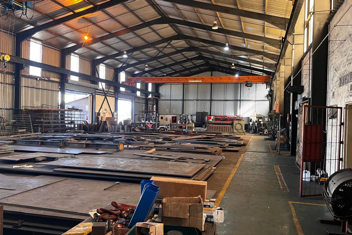 Spacious industrial warehouse featuring high ceilings, steel roof trusses, an overhead crane system, and durable concrete flooring, suitable for manufacturing or storage operations.