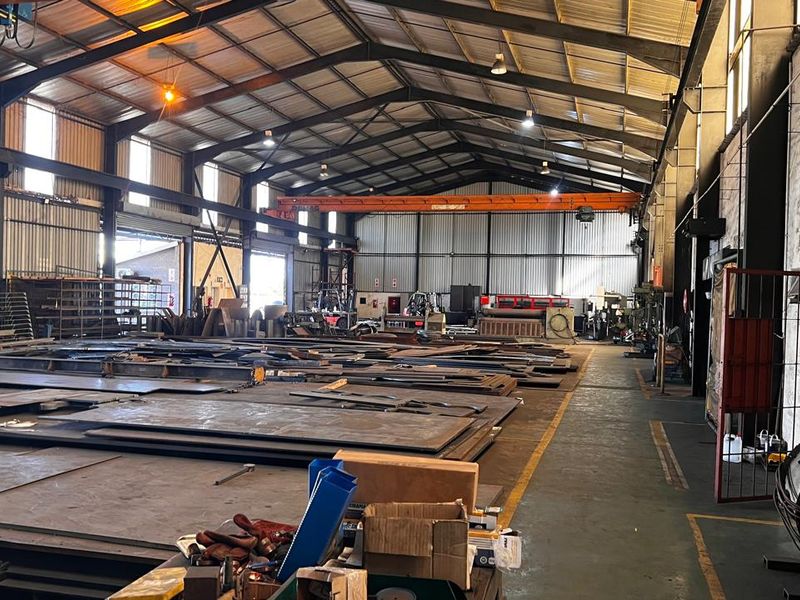 Spacious industrial warehouse featuring high ceilings, steel roof trusses, an overhead crane system, and durable concrete flooring, suitable for manufacturing or storage operations.