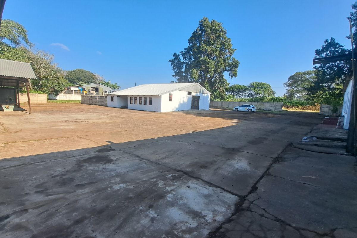 Spacious industrial yard featuring extensive concrete paving, perimeter walling, and a detached industrial building with a metal roof.