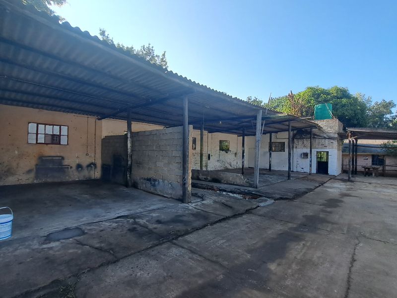 Expansive industrial outdoor area featuring a large covered workspace with concrete flooring, cinder block partitions, and a corrugated metal roof structure.