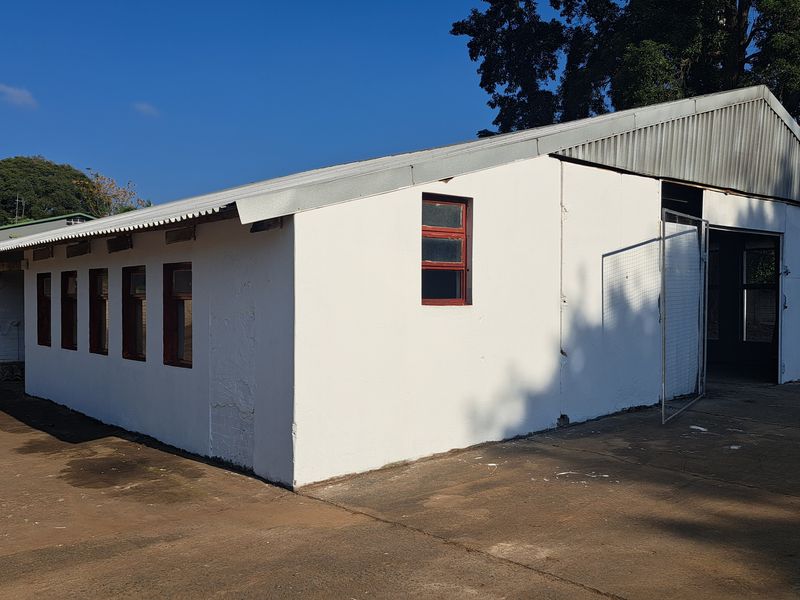 Industrial warehouse building featuring a corrugated metal roof, concrete apron, and multiple steel-framed windows, suitable for storage or light manufacturing operations.