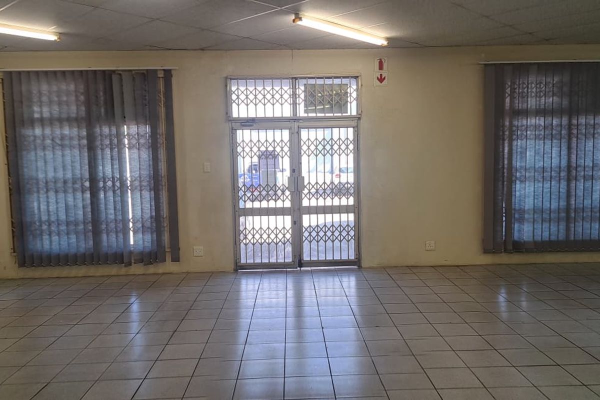 An open-plan retail space featuring tiled flooring, security gates, and large windows with vertical blinds, offering a blank canvas for commercial use.