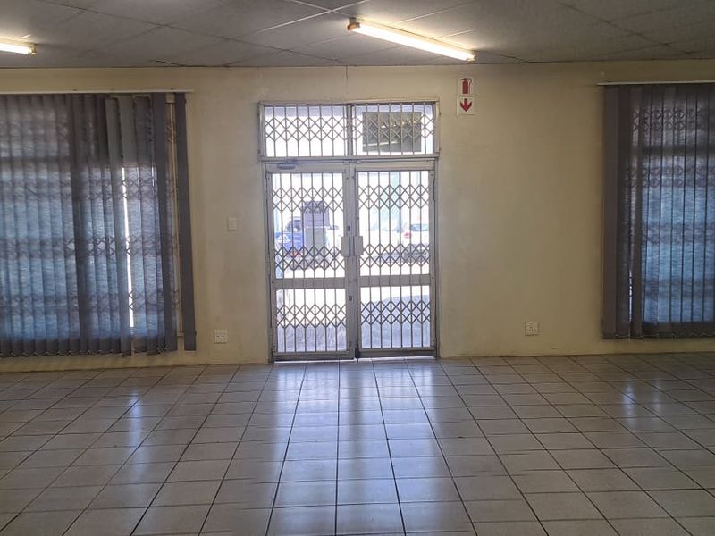 An open-plan retail space featuring tiled flooring, security gates, and large windows with vertical blinds, offering a blank canvas for commercial use.