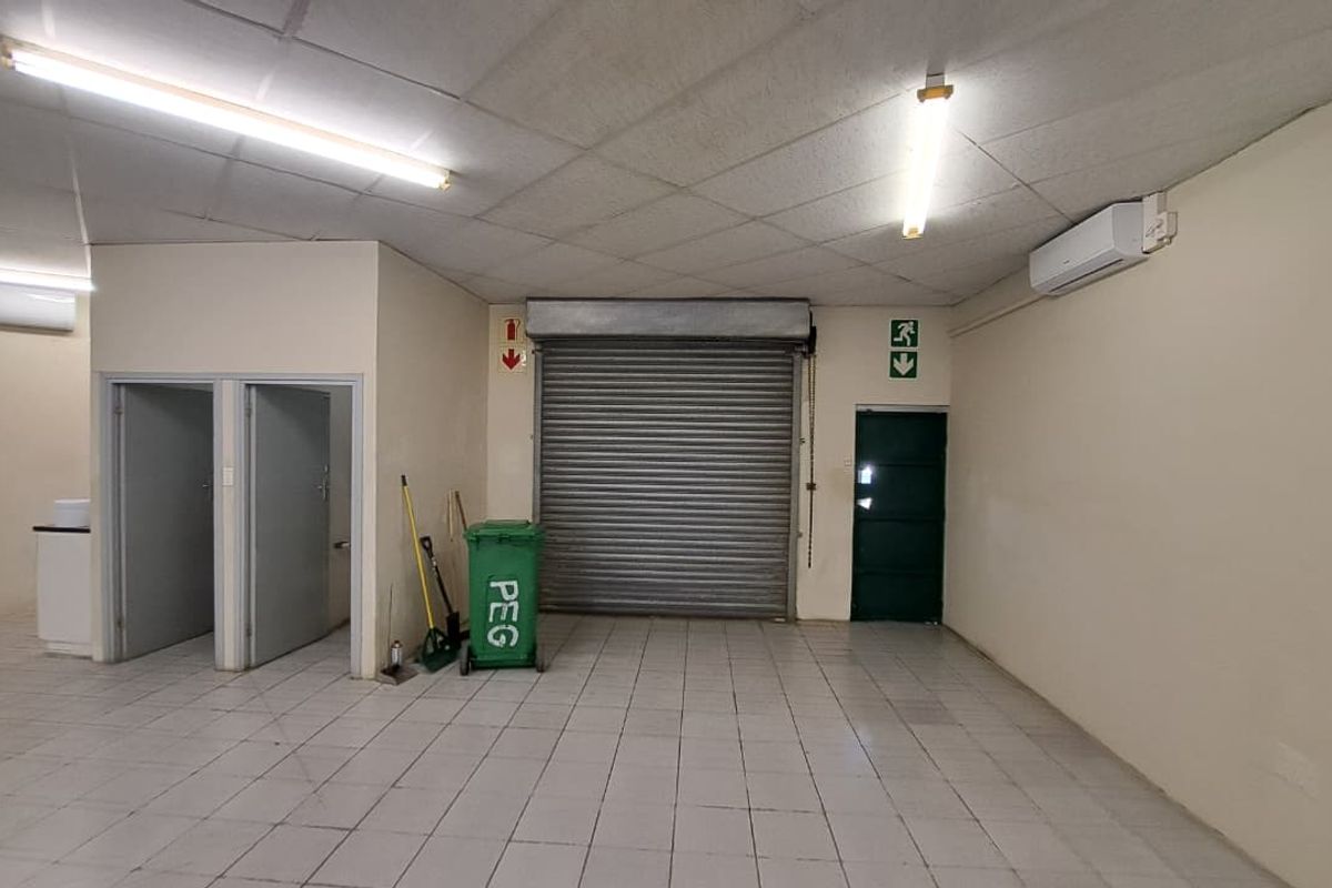 Open-plan utility or retail space featuring tiled flooring, a roller shutter door, split-system air conditioning, and functional overhead lighting.
