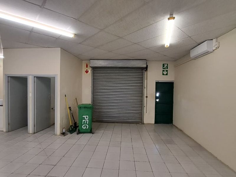Open-plan utility or retail space featuring tiled flooring, a roller shutter door, split-system air conditioning, and functional overhead lighting.