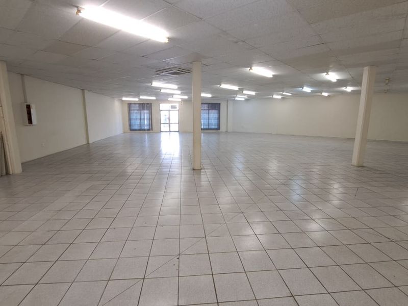 A large, vacant open-plan retail space featuring ceramic tiled flooring, structural columns, and a suspended ceiling with integrated lighting.
