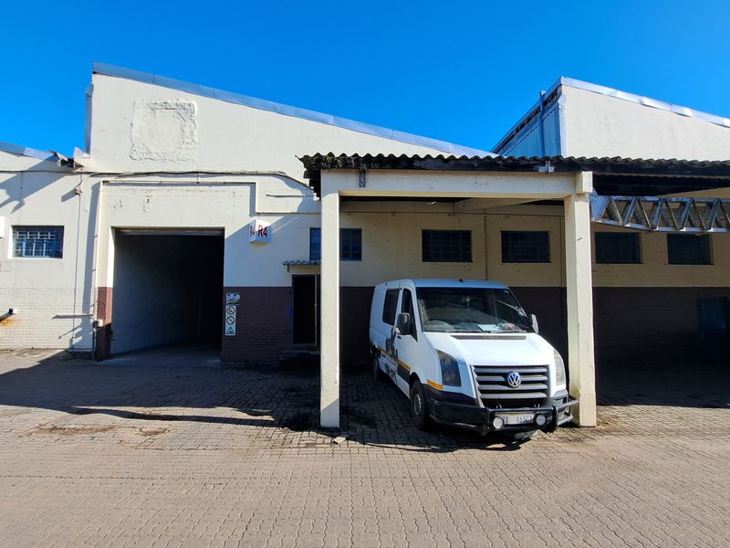 Industrial property exterior featuring a covered loading bay, paved driveway, and multiple access points for commercial operations.
