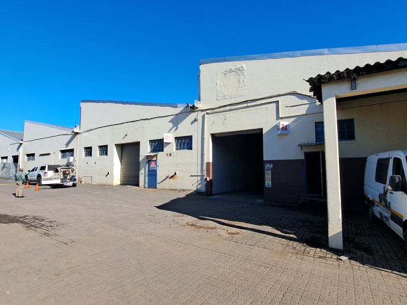 Front exterior view of an industrial warehouse complex featuring multiple roller shutter doors, a paved driveway, and a covered loading area.