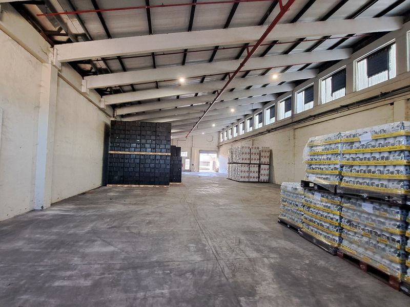 Spacious industrial warehouse featuring high ceilings with exposed steel trusses, concrete flooring, fire sprinkler system, and natural light from high-level clerestory windows.