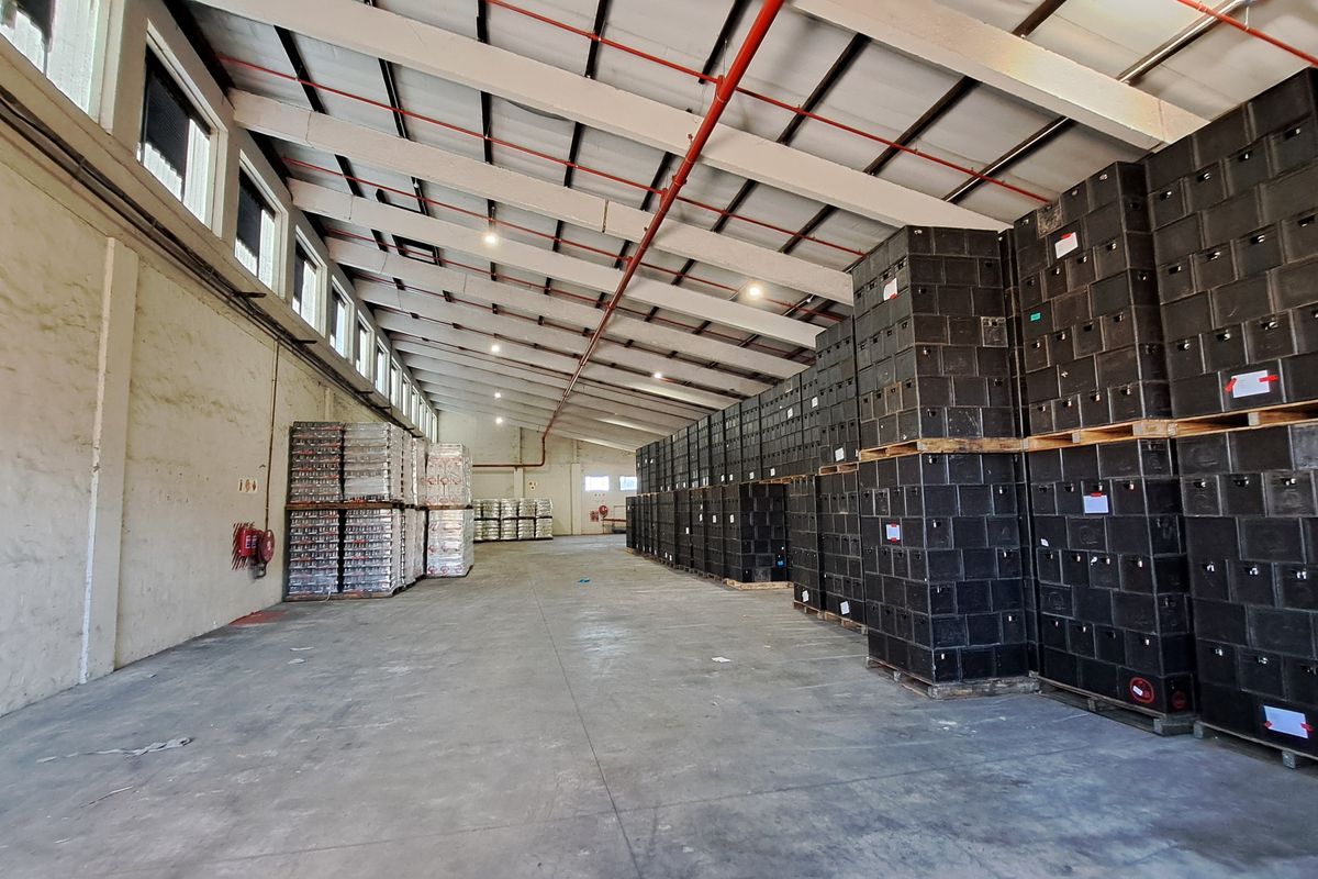 Spacious industrial warehouse featuring high ceilings with exposed steel trusses, fire sprinkler system, concrete flooring, and ample natural light from clerestory windows.