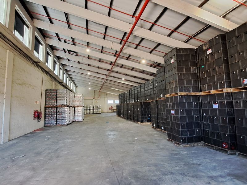 Spacious industrial warehouse featuring high ceilings with exposed steel trusses, fire sprinkler system, concrete flooring, and ample natural light from clerestory windows.