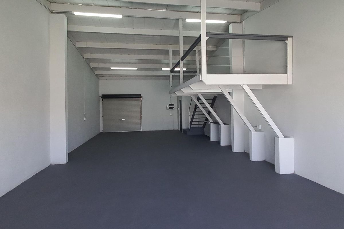 Spacious industrial unit featuring a mezzanine level, roller shutter door access, and high ceilings with integrated lighting, suitable for various commercial or storage uses.