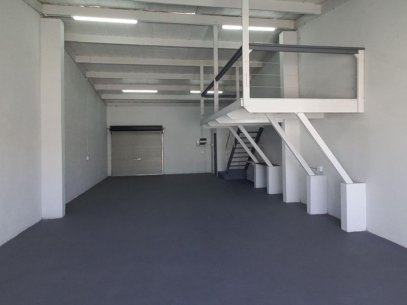 Spacious industrial unit featuring a mezzanine level, roller shutter door access, and high ceilings with integrated lighting, suitable for various commercial or storage uses.