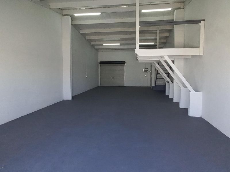 Spacious industrial unit featuring a clean painted concrete floor, high ceilings with fluorescent lighting, a roller shutter door, and an integrated mezzanine level.