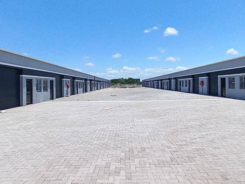A wide view of an industrial complex featuring rows of warehouse units with roller shutter doors and a central paved driveway.