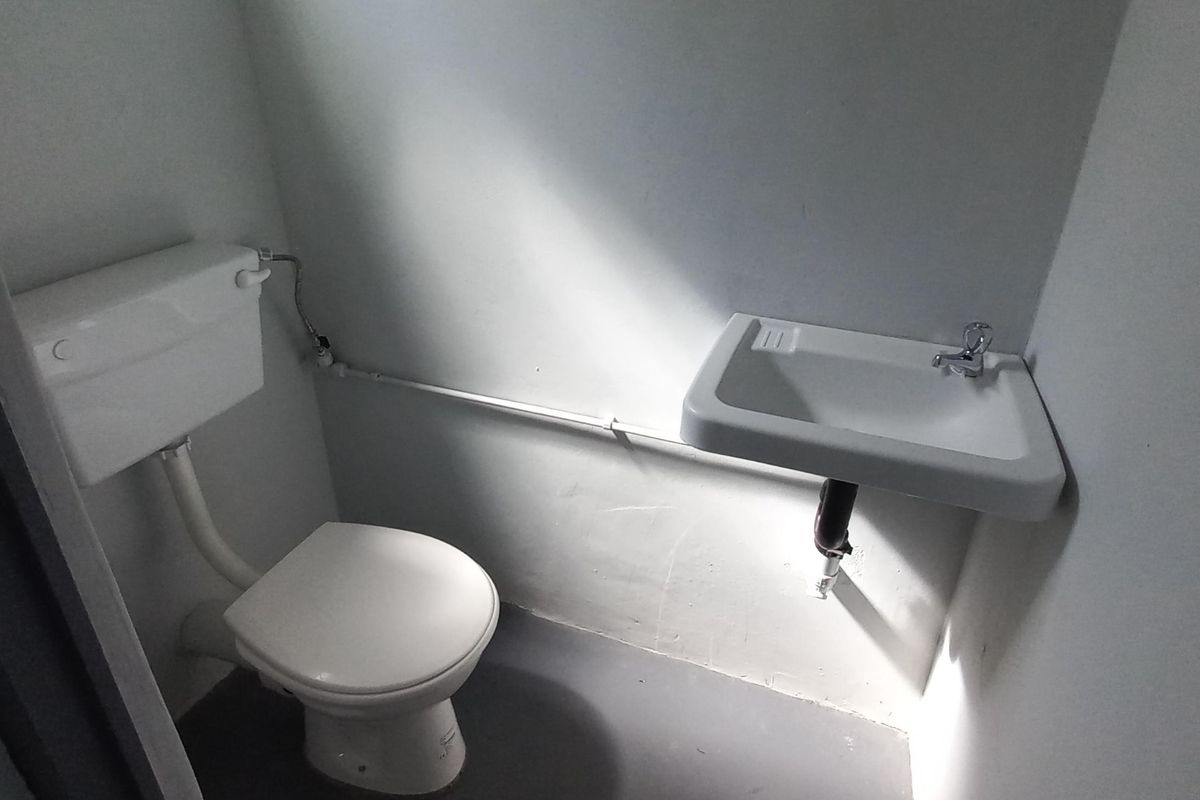 A compact industrial-style bathroom featuring a standard toilet and a wall-mounted basin with exposed plumbing.