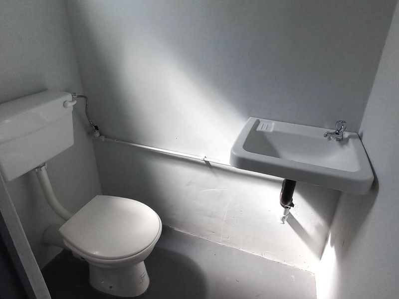 A compact industrial-style bathroom featuring a standard toilet and a wall-mounted basin with exposed plumbing.