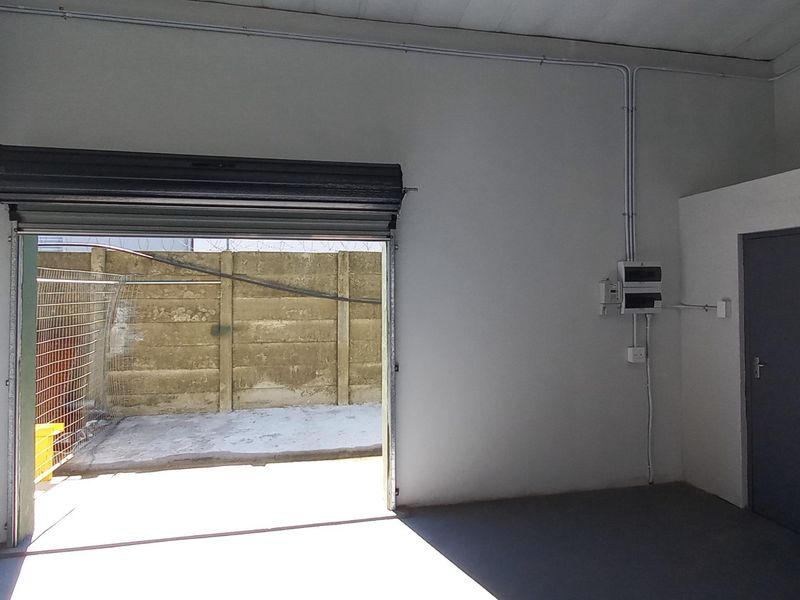 A clean, empty industrial garage space featuring a roller shutter door, exposed electrical conduit, and durable concrete flooring.