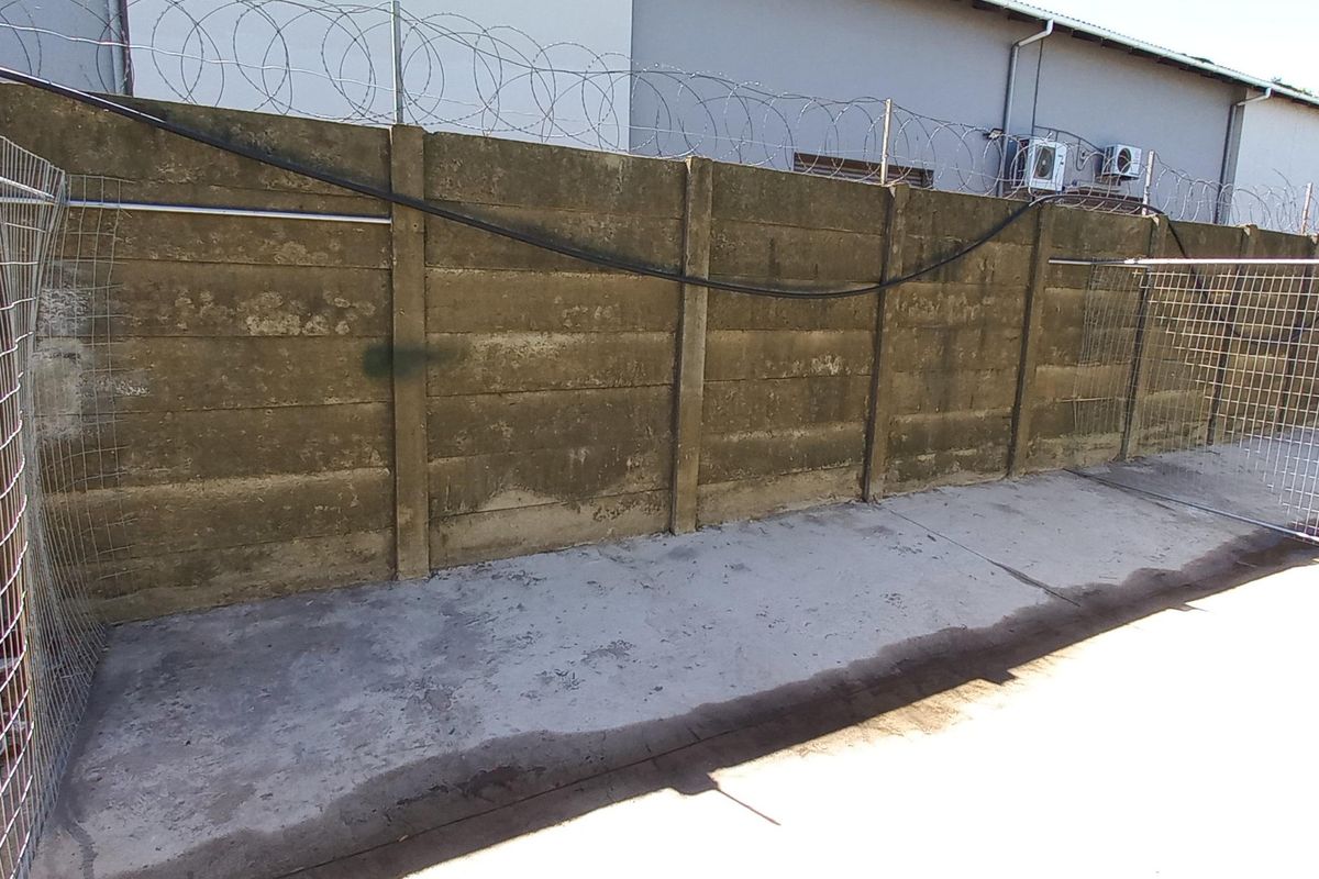 Rear industrial yard area featuring a high precast concrete boundary wall topped with razor wire and concrete paved flooring.