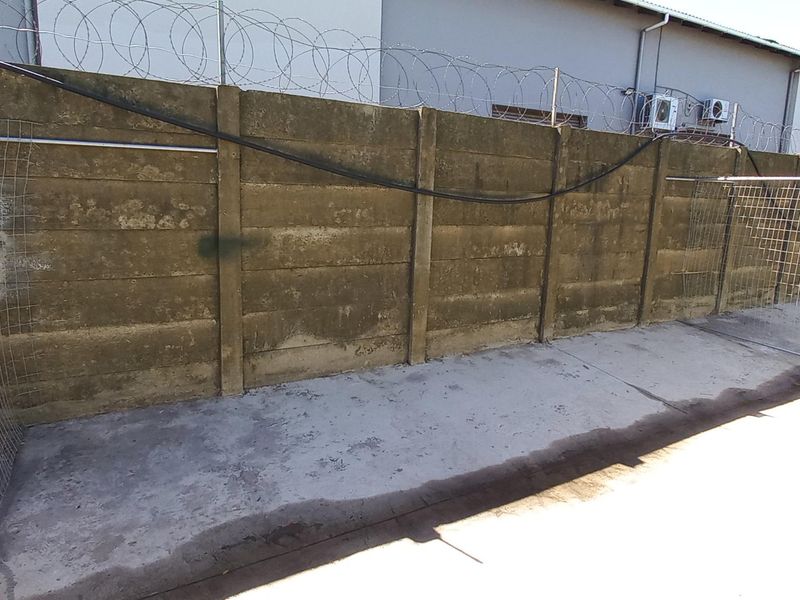 Rear industrial yard area featuring a high precast concrete boundary wall topped with razor wire and concrete paved flooring.