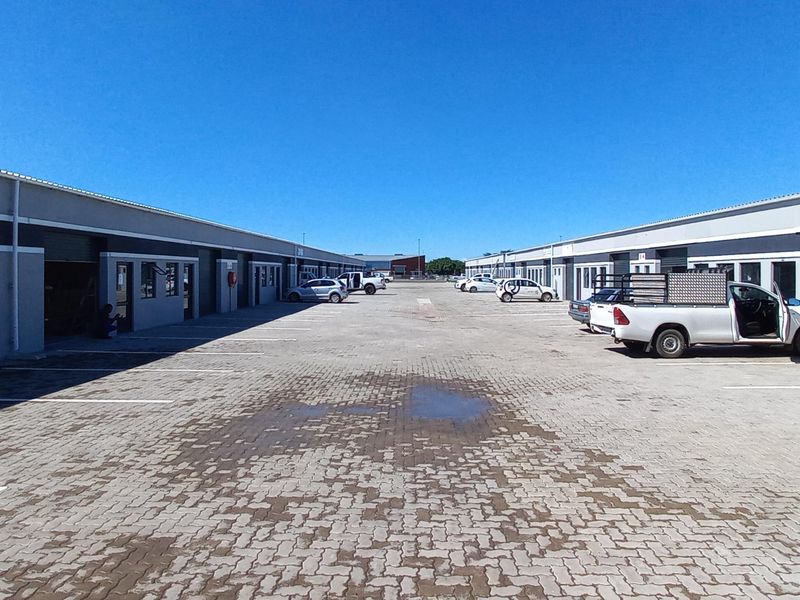 Exterior view of an industrial complex featuring multiple units with roller shutter doors and a paved parking area.