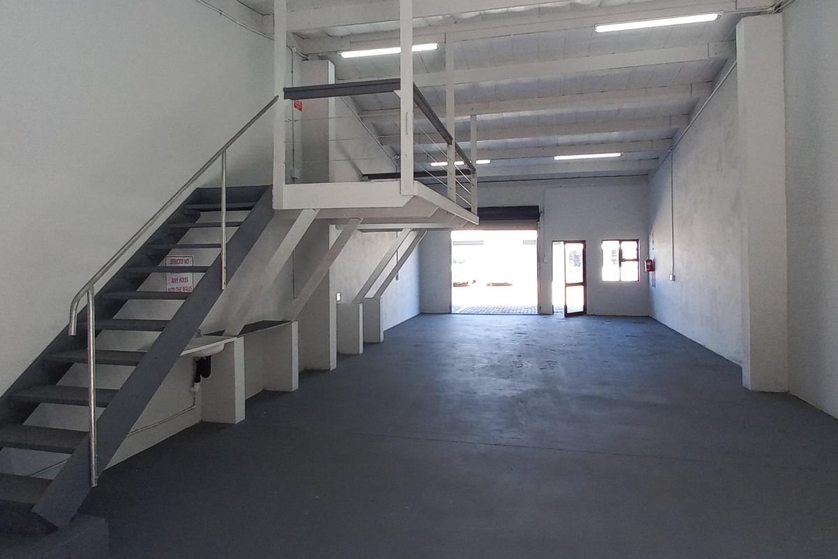 Spacious industrial warehouse unit featuring a mezzanine level, concrete flooring, roller shutter access, and functional overhead lighting.