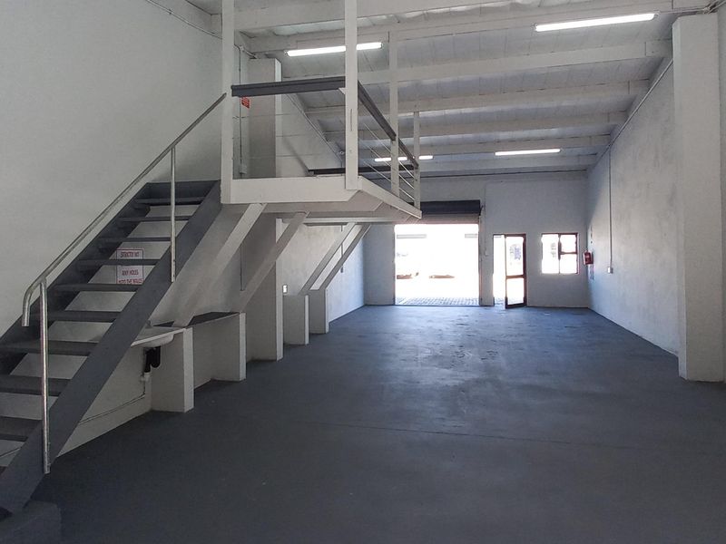 Spacious industrial warehouse unit featuring a mezzanine level, concrete flooring, roller shutter access, and functional overhead lighting.
