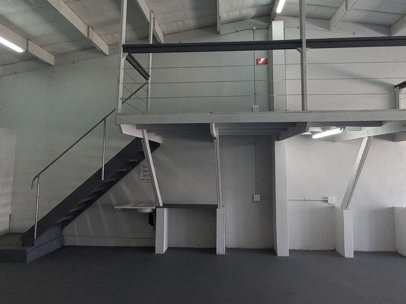 Industrial utility space featuring a mezzanine level with steel staircase, exposed ceiling beams, and functional wall-mounted electrical and plumbing fixtures.