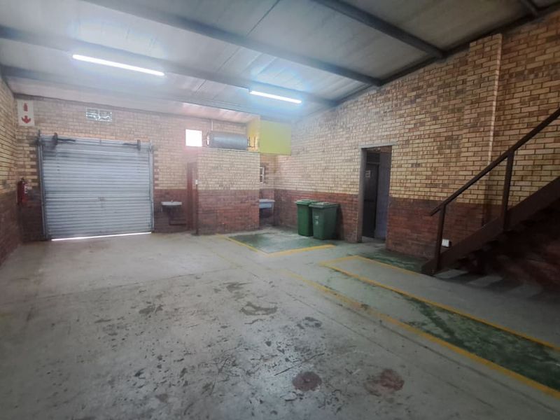 Spacious industrial garage featuring exposed brick walls, a roller shutter door, concrete flooring, and an internal metal staircase.