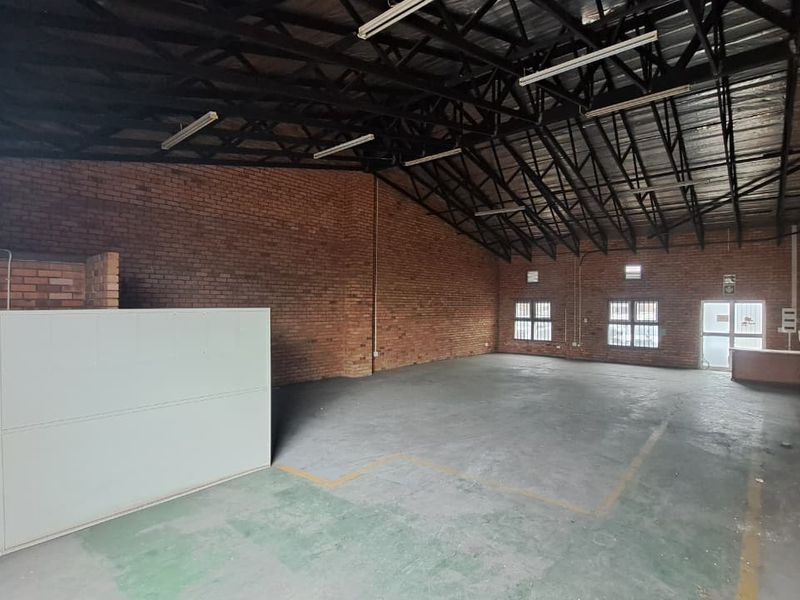 Spacious industrial utility area featuring exposed brick walls, high steel roof trusses, concrete flooring, and functional fluorescent lighting.