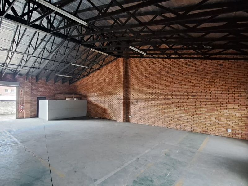 Spacious industrial utility area featuring exposed brick walls, high steel truss ceilings, concrete flooring, and a large roller shutter door for easy access.