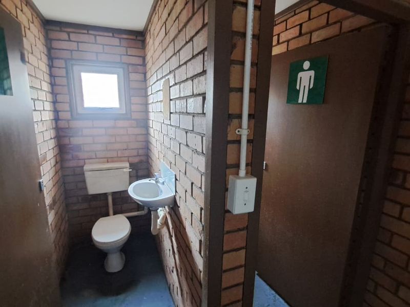 Functional industrial-style restroom facility featuring exposed brick walls, a wall-mounted basin, and a standard toilet.