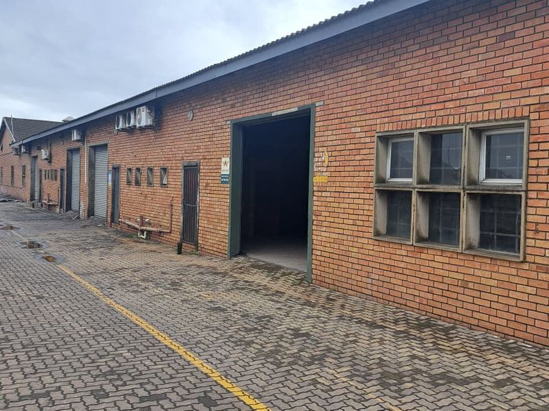 Rear exterior view of an industrial warehouse facility featuring brick construction, multiple roller shutter access points, and a paved yard area.