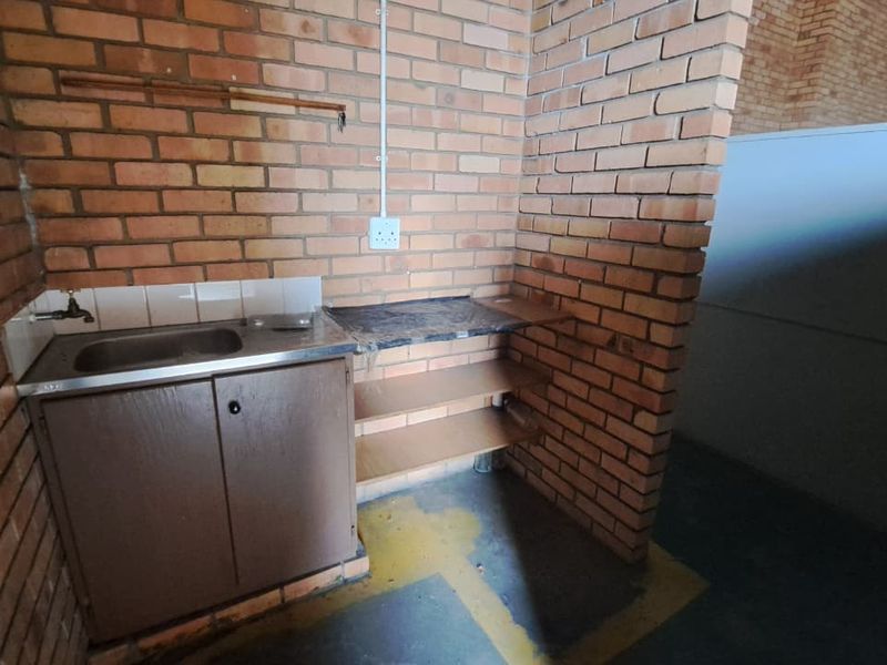 A functional industrial scullery area featuring exposed brick walls, a stainless steel sink, built-in cabinetry, and open shelving for storage.